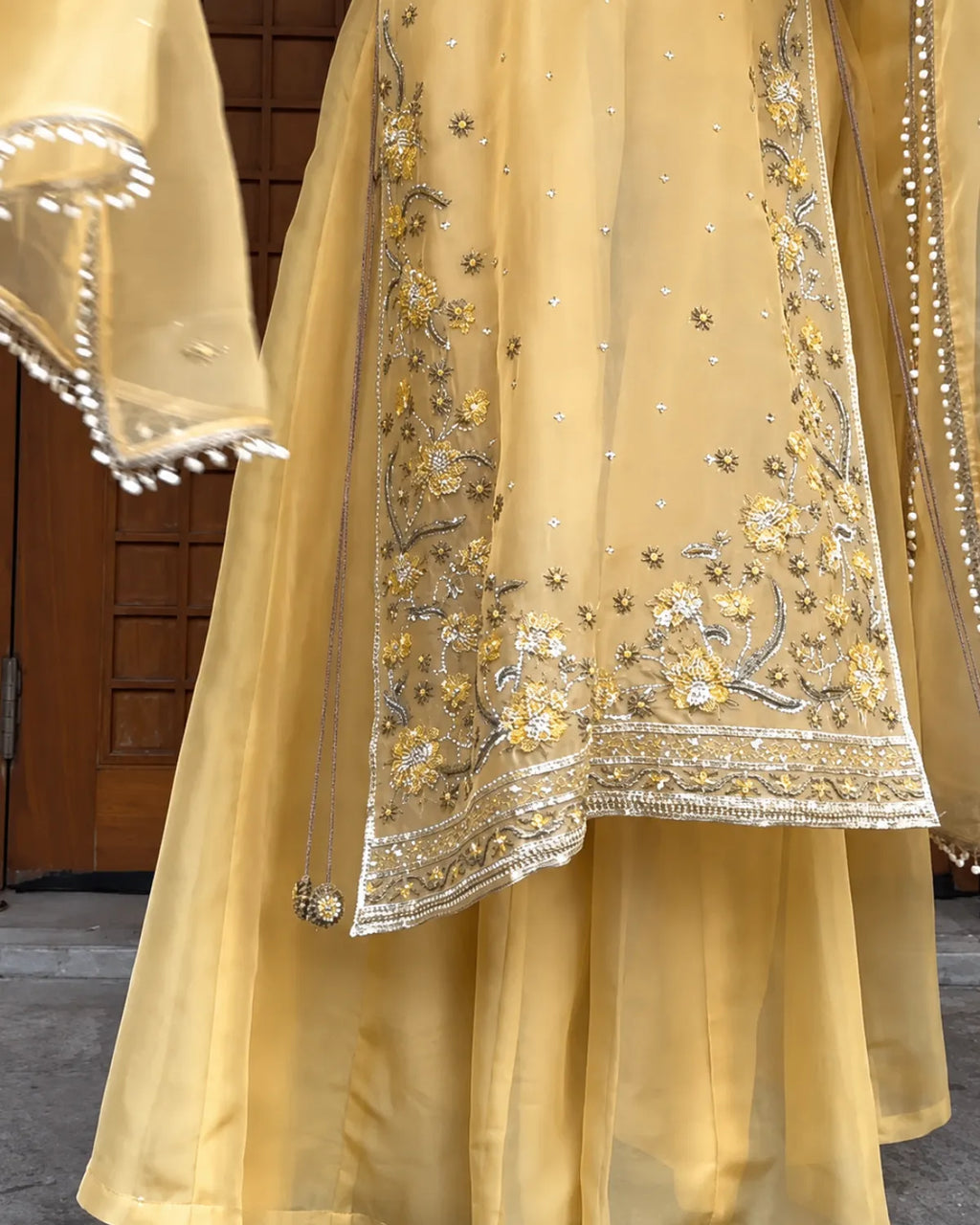 A close-up of a flowing yellow traditional outfit with detailed gold and silver floral embroidery and beadwork on the fabric panels.