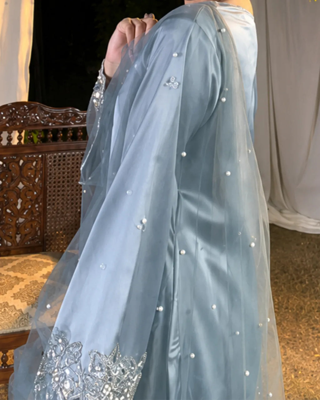 A light blue satin and organza traditional outfit with silver mirror work embroidery and pearl embellishments, shown on a model in an indoor setting.