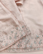 Close-up of a light blush pink fabric garment with detailed silver and white floral embroidery along the hem and sleeve.