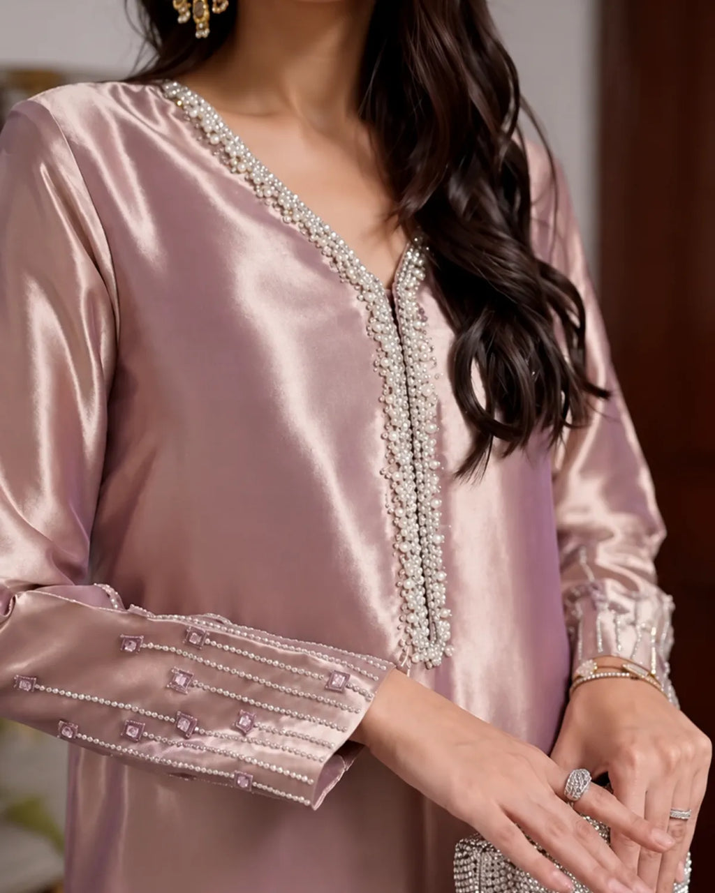 A close-up of a woman wearing a light pink satin kurta with intricate silver and white beaded embellishments along the V-neckline and cuffs.