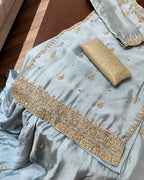 A light blue satin ethnic outfit with gold embroidery and a matching gold clutch purse, laid out on a dark wooden surface.