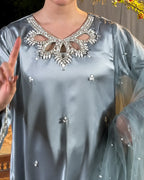 A close-up of a person wearing a light blue satin tunic top with a heavily embellished silver rhinestone V-neckline and small scattered rhinestone accents on the fabric and sheer sleeves.