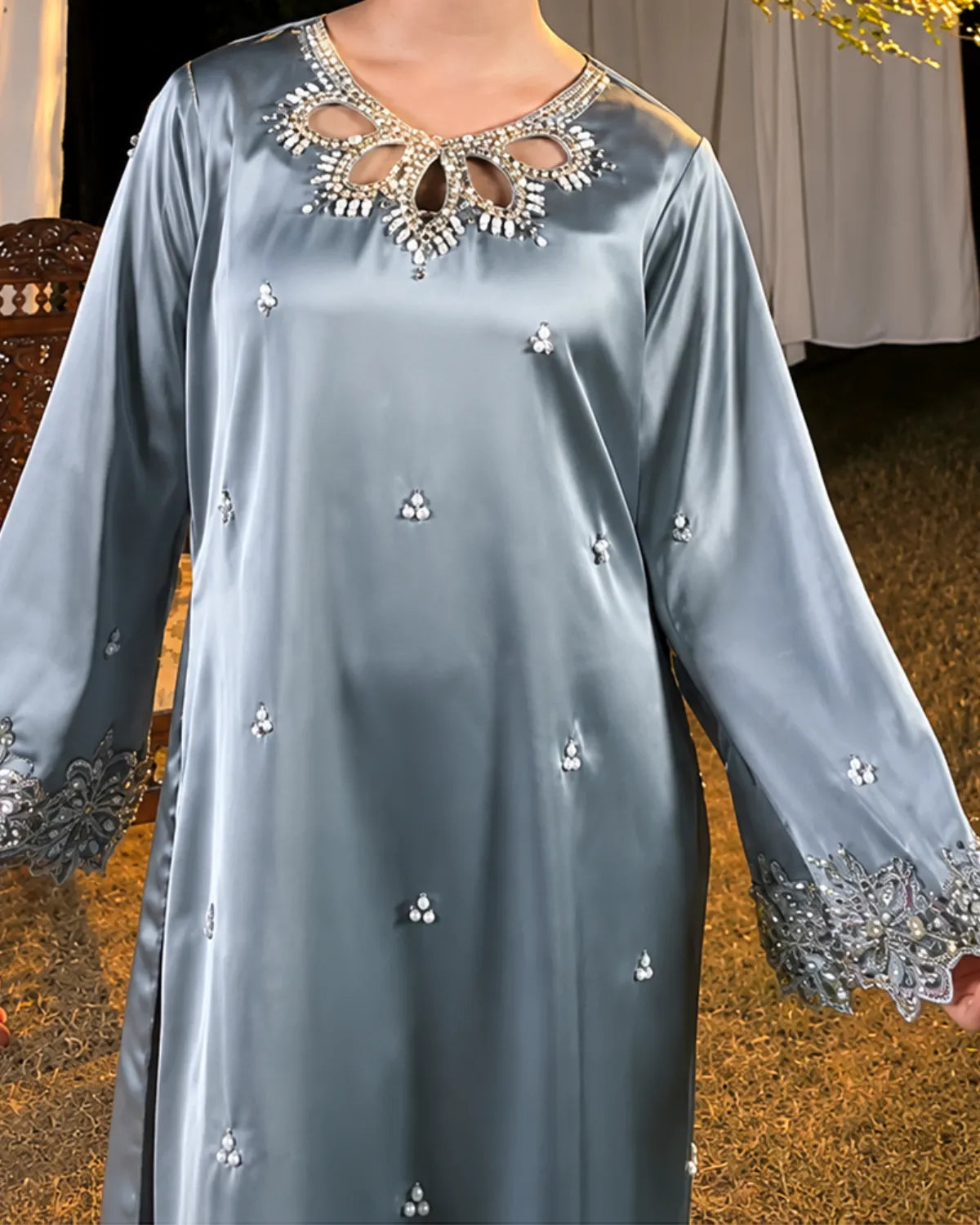 A light blue satin caftan with intricate silver and white beadwork around the V-neck and sleeve cuffs, shown on a model in an outdoor setting.