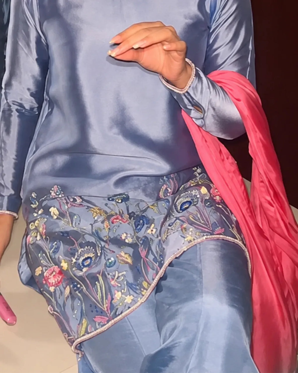 A close-up of a person wearing a light blue satin three-piece outfit with floral embroidered details on the bottom, paired with a bright pink dupatta.