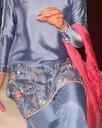 A close-up of a person wearing a light blue satin three-piece outfit with floral embroidered details on the bottom, paired with a bright pink dupatta.