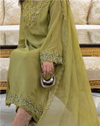 A woman wearing a sage green traditional outfit with floral embroidery and a matching sheer dupatta, holding a metallic silver crescent-shaped handbag in an indoor setting.