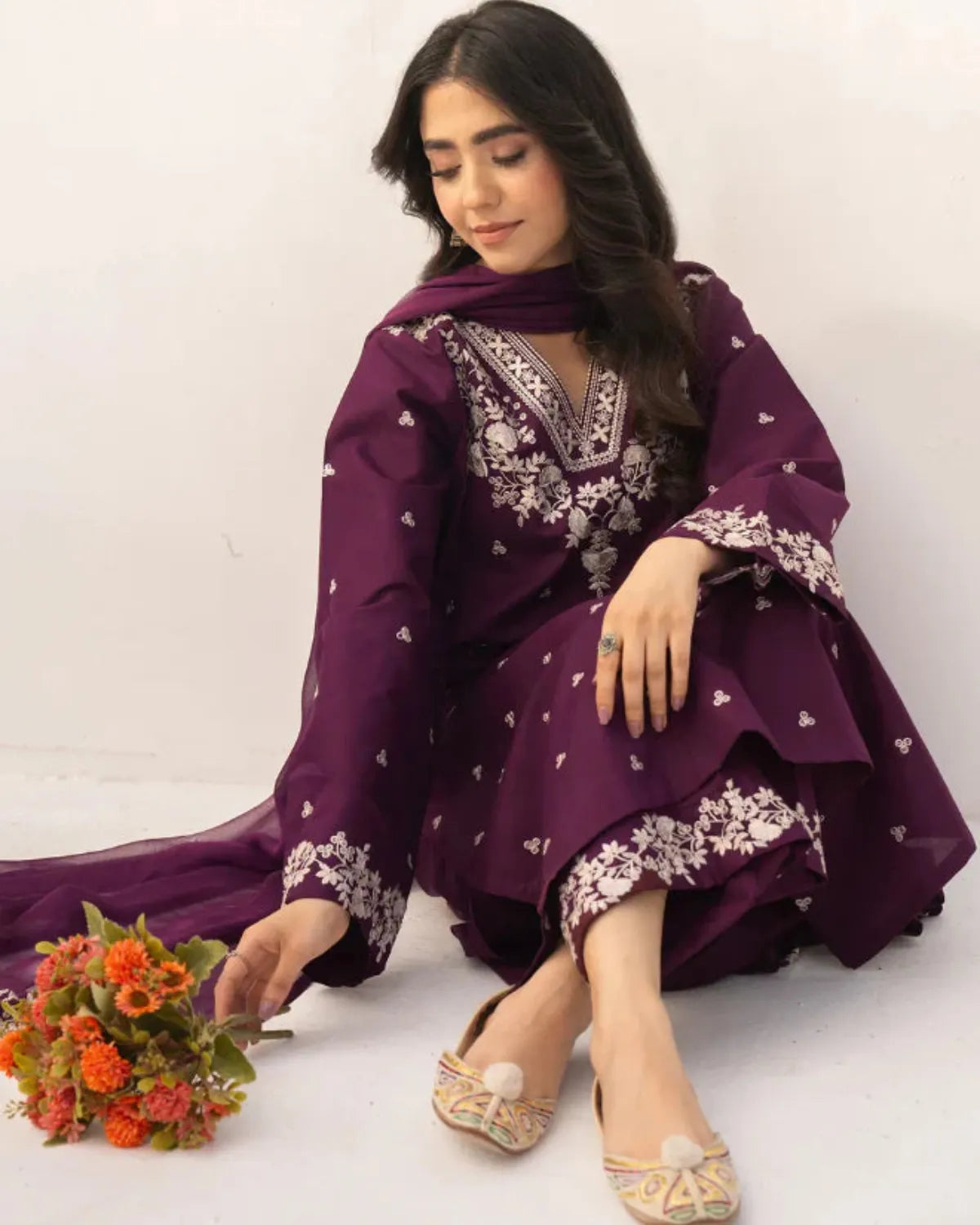 Woman in a purple traditional outfit with floral patterns sitting on a white background