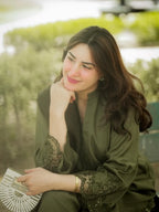 Woman in a green outfit sitting outdoors with trees in the background