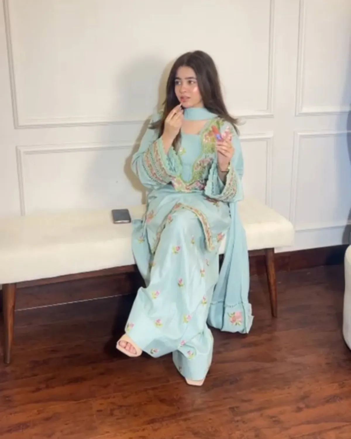 Woman in a light blue traditional outfit sitting on a white bench indoors.