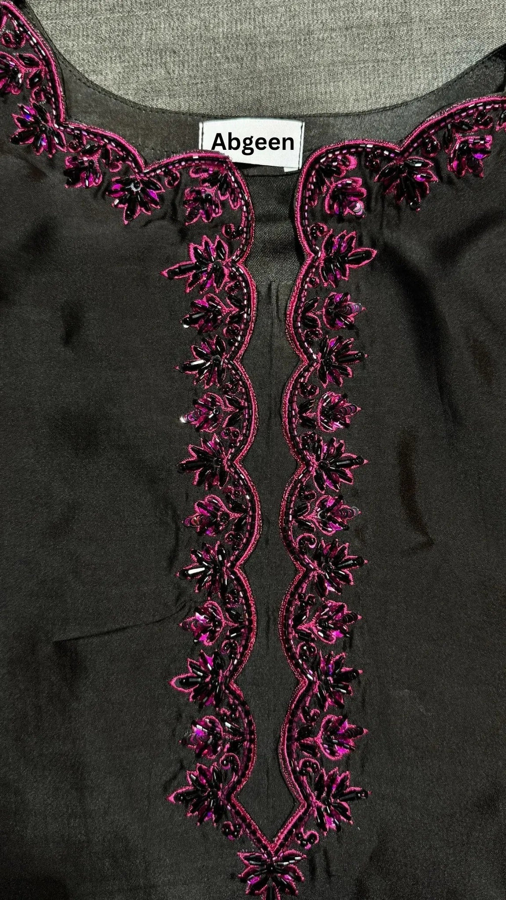 Black garment with pink embroidery and 'Abgeen' label on a gray background