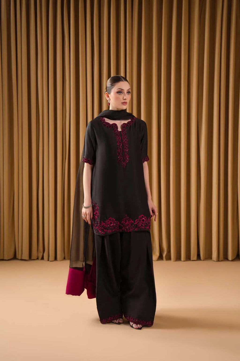Woman wearing a black and red embroidered outfit against a beige curtain background