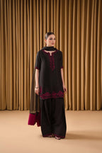 Woman wearing a black and red embroidered outfit against a beige curtain background