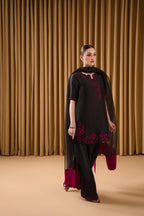 Woman wearing a black outfit with red embroidery against a beige curtain background