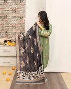 Woman holding a floral-patterned saree in a room with a newspaper wall and oranges on the floor.
