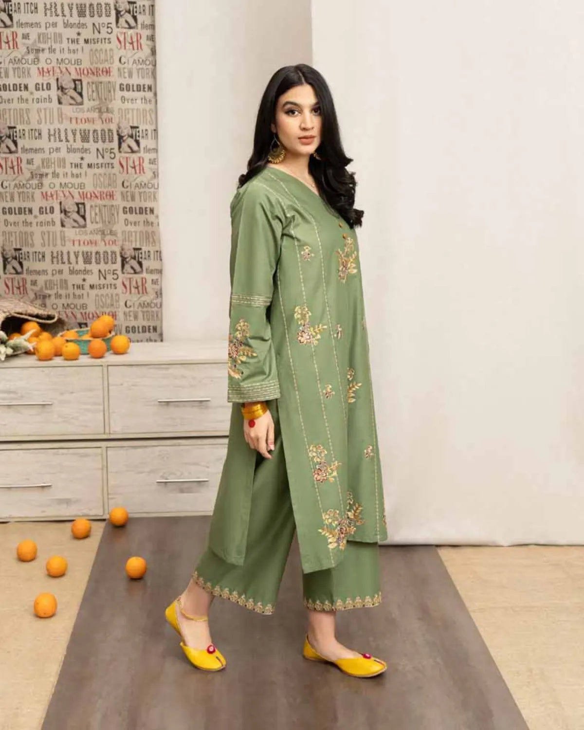 Woman in a green embroidered outfit standing in a room with decorative elements.