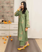 Woman in a green embroidered outfit standing in a room with a decorative wall and scattered oranges on the floor.