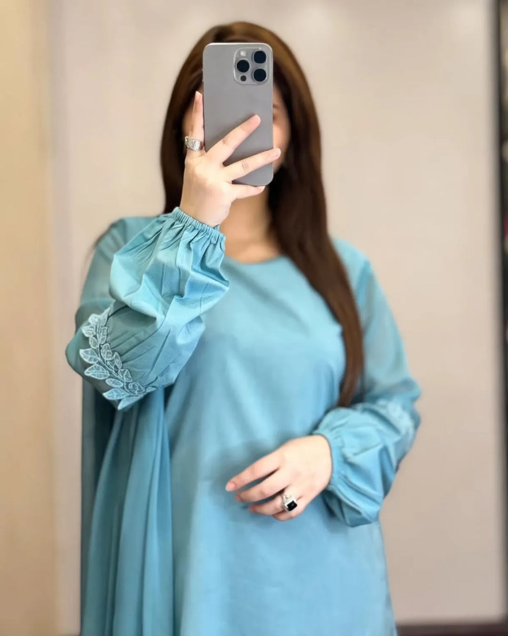 Person wearing a light blue dress with sheer sleeves against a plain background
