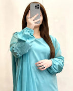 Person wearing a light blue dress with floral embroidery, taking a mirror selfie.