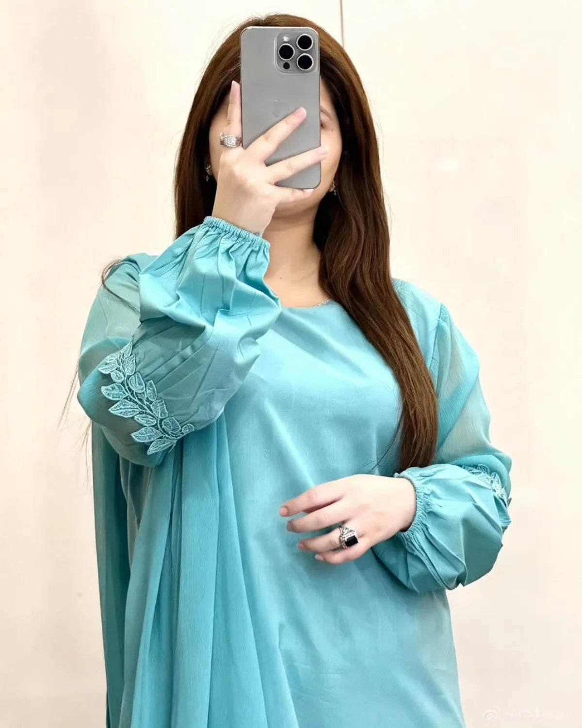 Person wearing a light blue dress with floral embroidery, taking a mirror selfie.