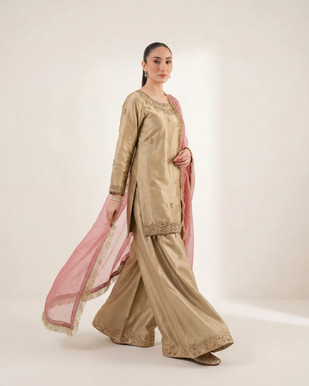 Woman wearing a traditional beige outfit with a pink dupatta on a white background