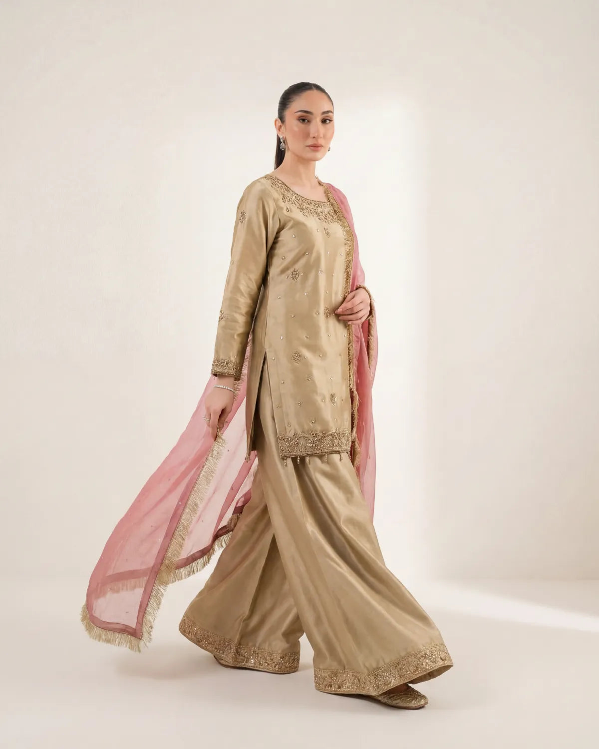 Woman wearing a traditional beige outfit with a pink dupatta on a white background
