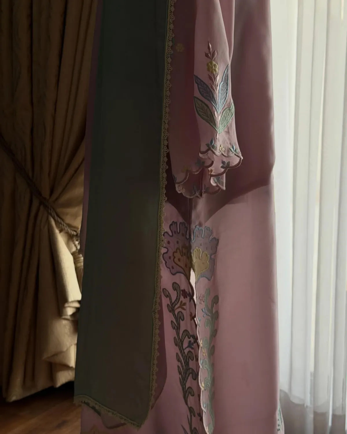 Pink garment with floral embroidery hanging against a neutral background