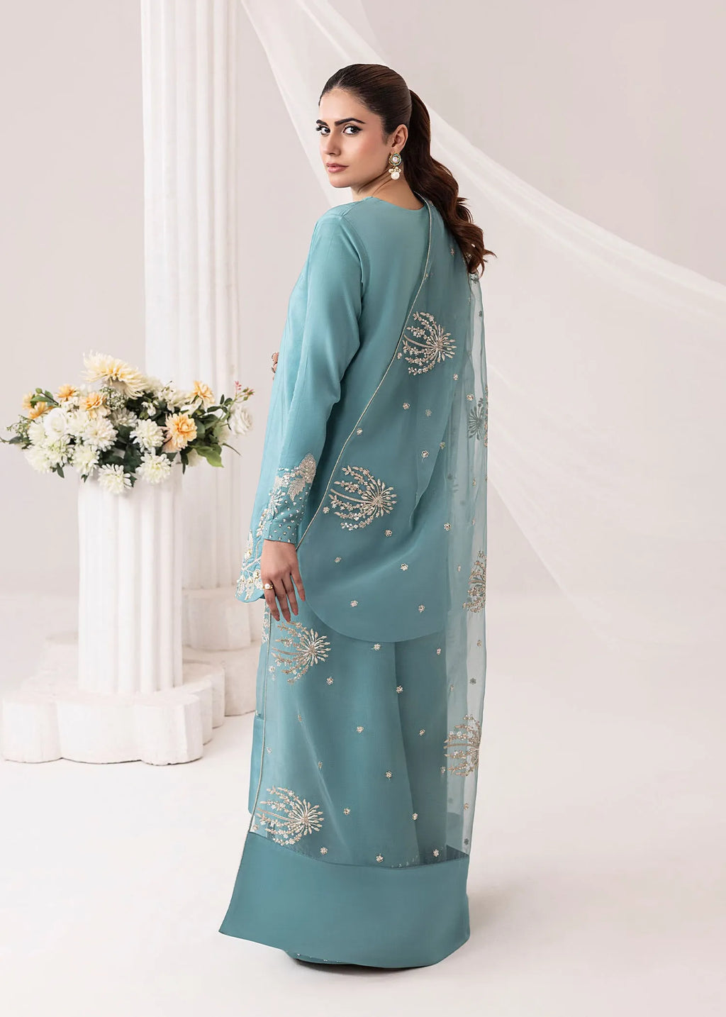 Woman wearing a teal embroidered outfit with a white background