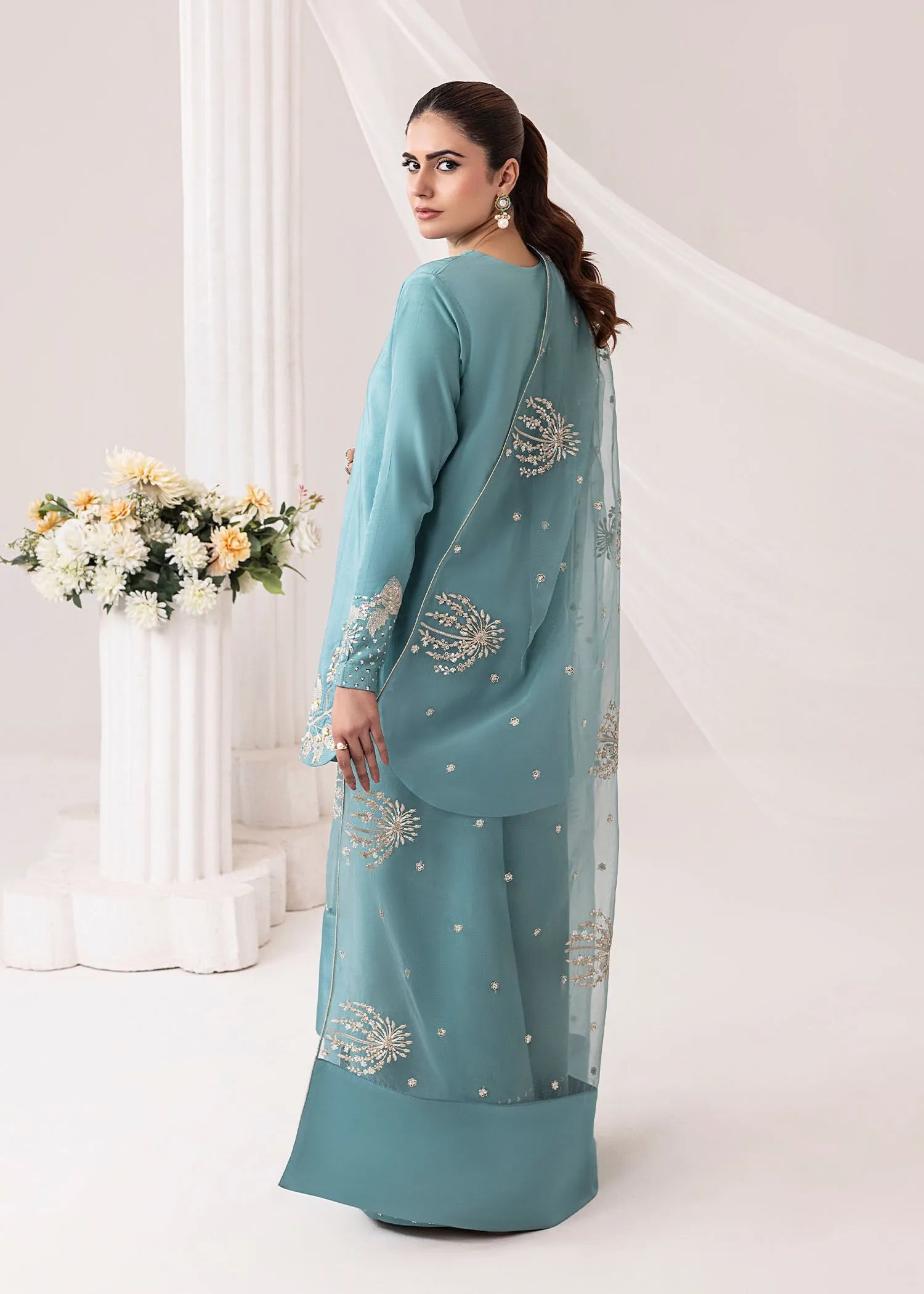 Woman wearing a teal embroidered outfit with a white background