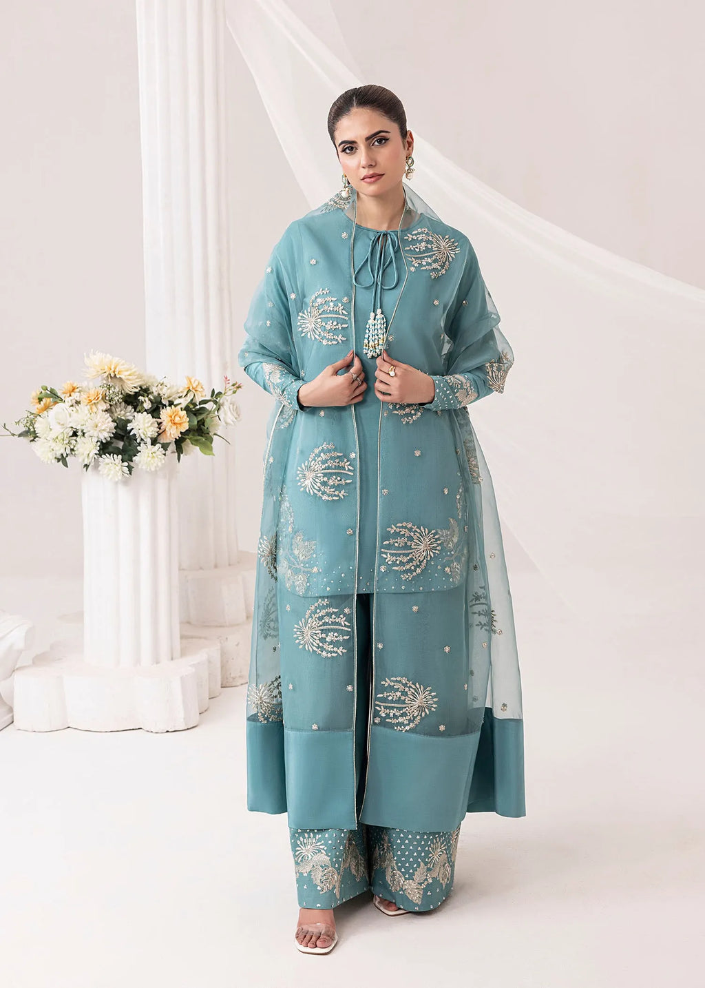 Woman wearing a light blue embroidered traditional outfit with a white background