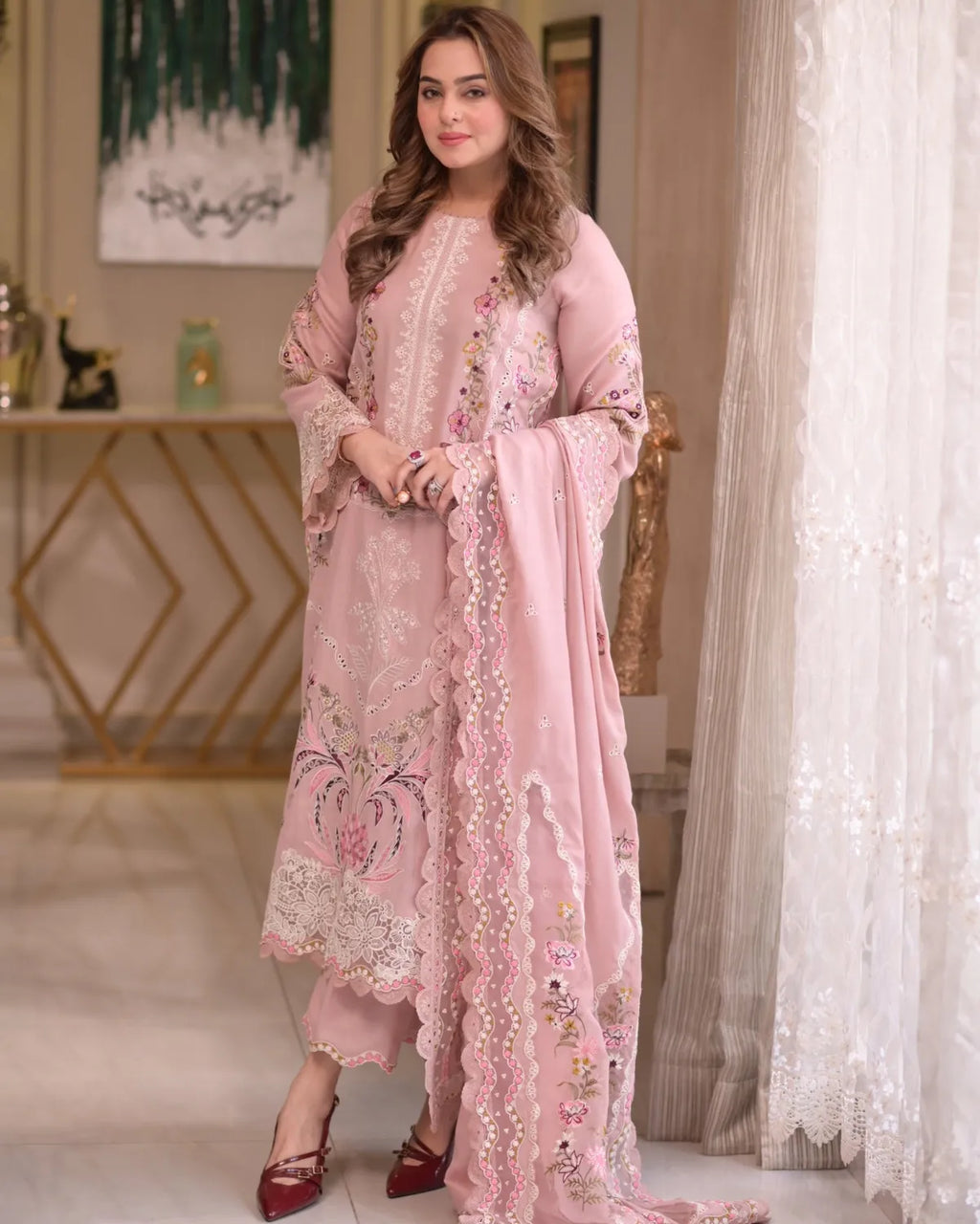 Woman wearing a pink embroidered outfit in an elegant room.
