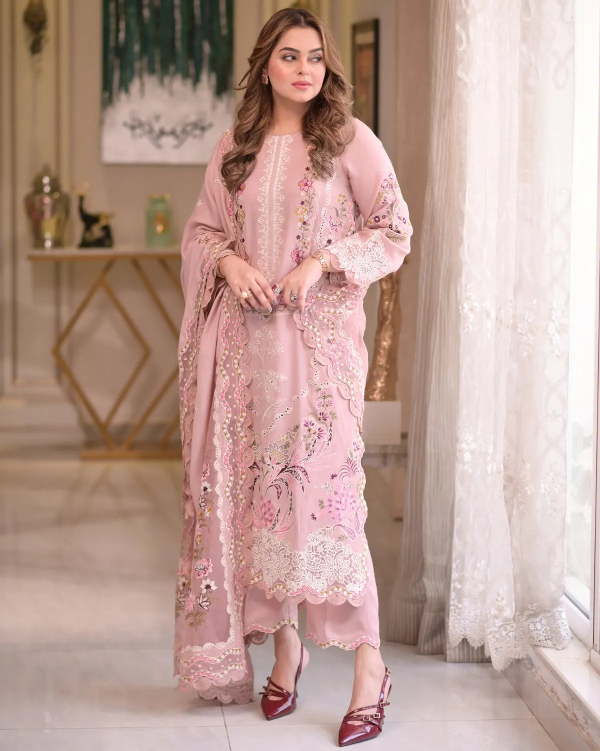 Woman in a pink embroidered outfit standing in a decorated room.