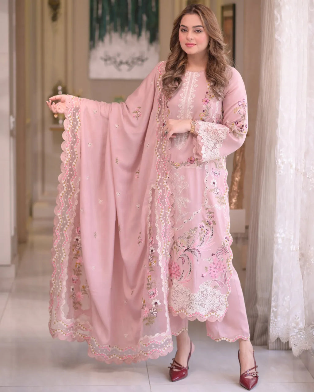Woman wearing a pink embroidered outfit with a matching dupatta in an indoor setting.