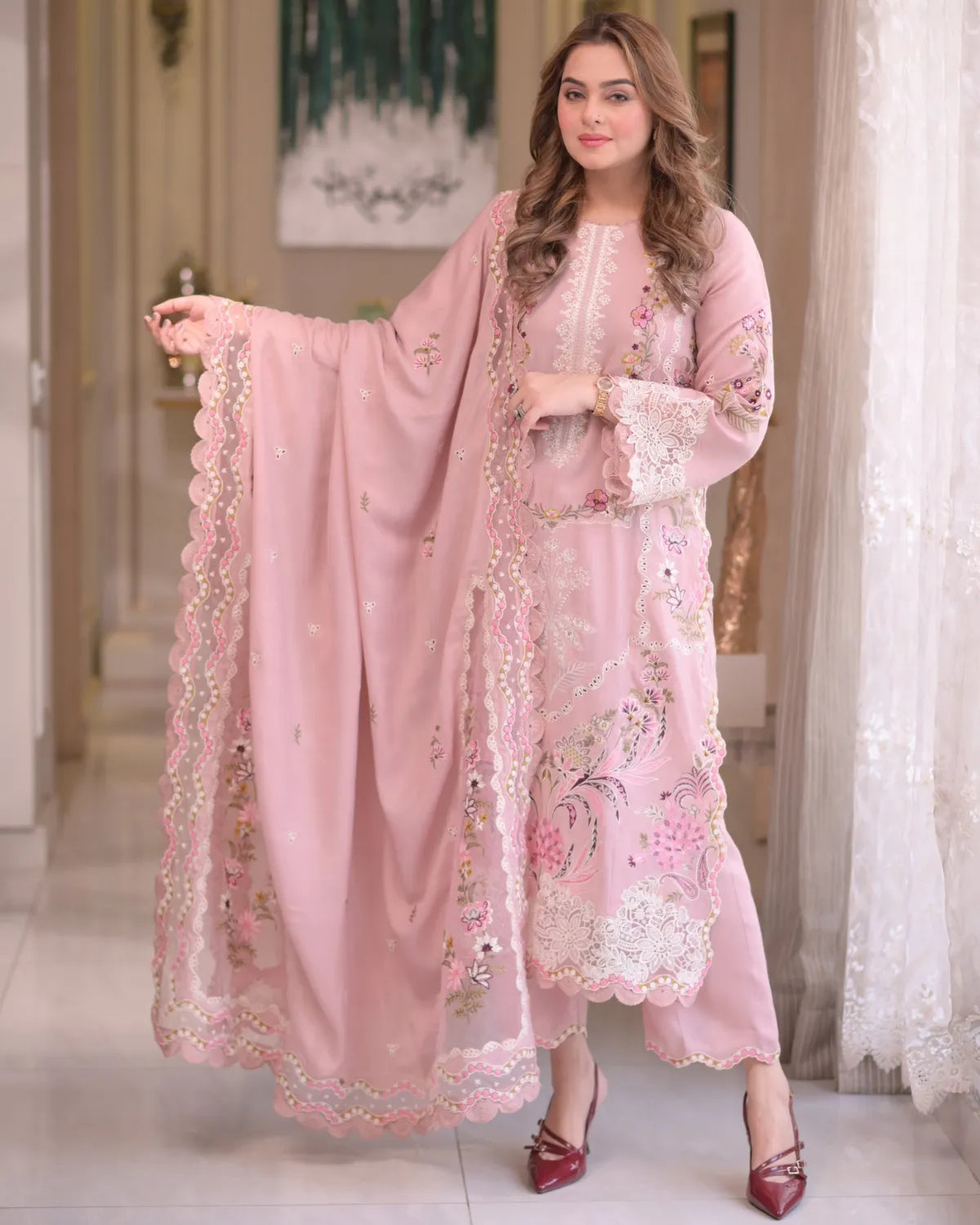 Woman wearing a pink embroidered outfit with a matching dupatta in an indoor setting.