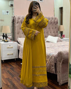 Woman wearing a yellow dress with intricate patterns in a bedroom setting.