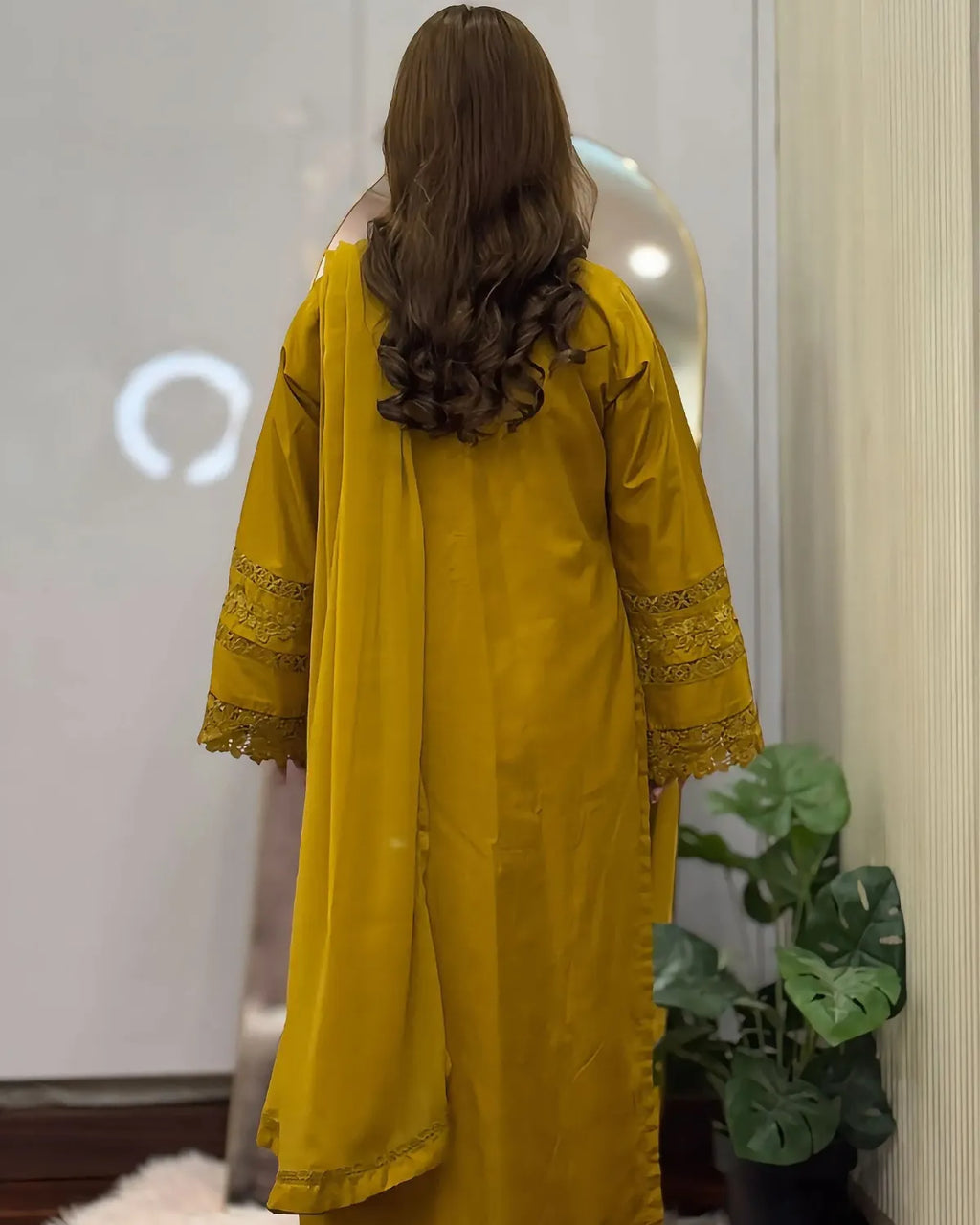 Person wearing a yellow outfit with lace details in a room with a plant.