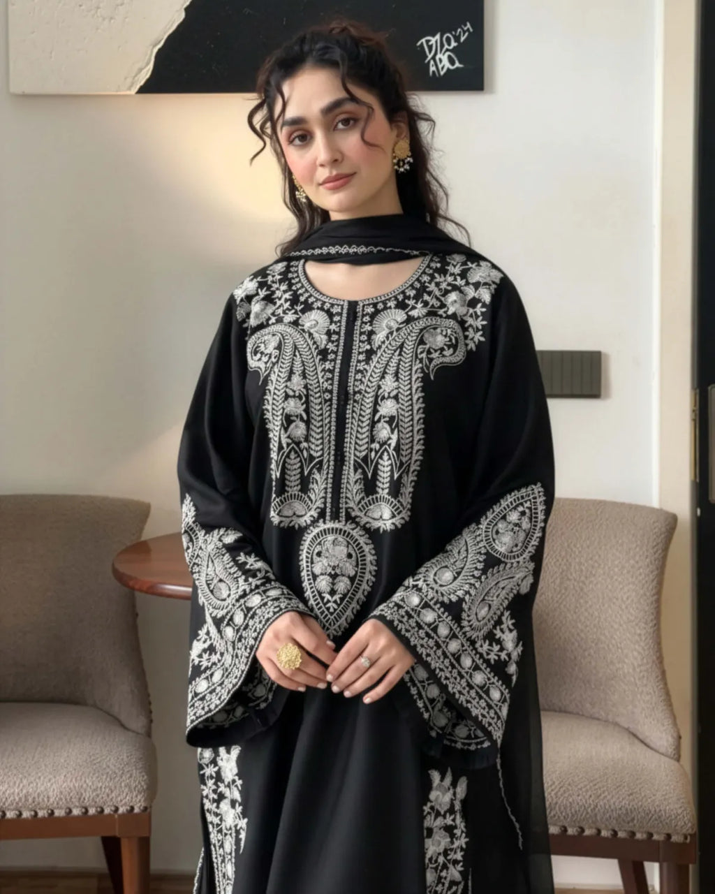 Woman wearing a black and white embroidered traditional outfit indoors.