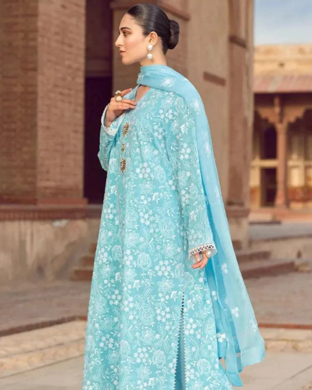 Woman in a light blue traditional outfit standing outdoors with architectural background
