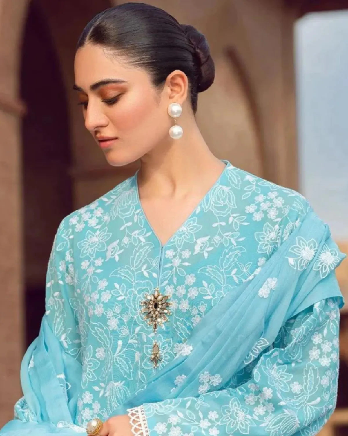 Woman wearing a light blue saree with white floral patterns, set against a blurred background.