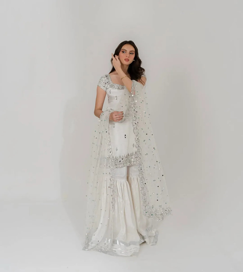 Woman wearing a white saree with silver embroidery on a plain background