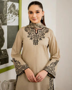 Woman wearing a beige dress with black embroidery in an indoor setting.