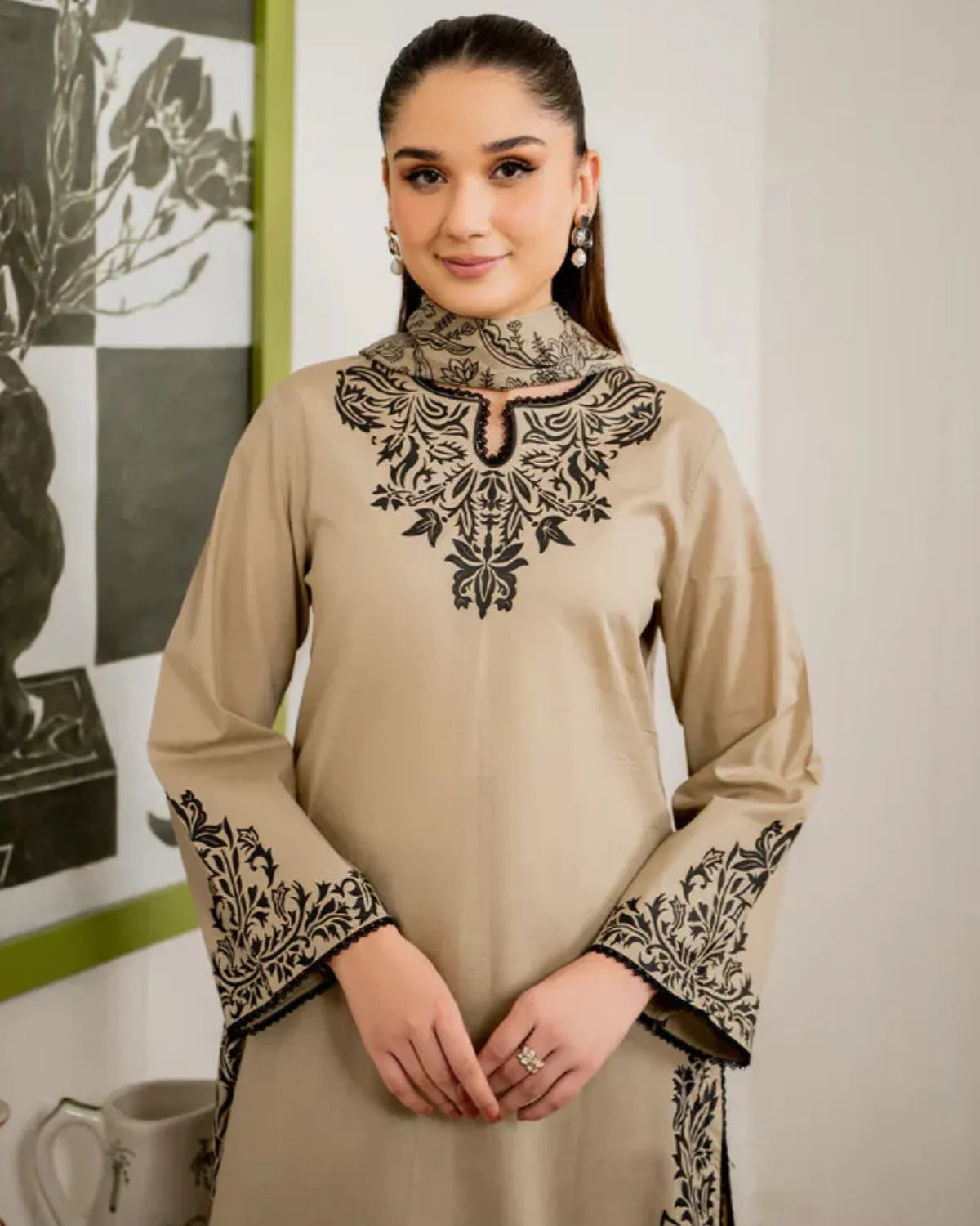 Woman wearing a beige dress with black embroidery in an indoor setting.