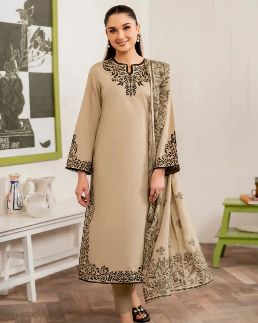 Woman wearing a beige embroidered outfit in a room with a white wall and green table.