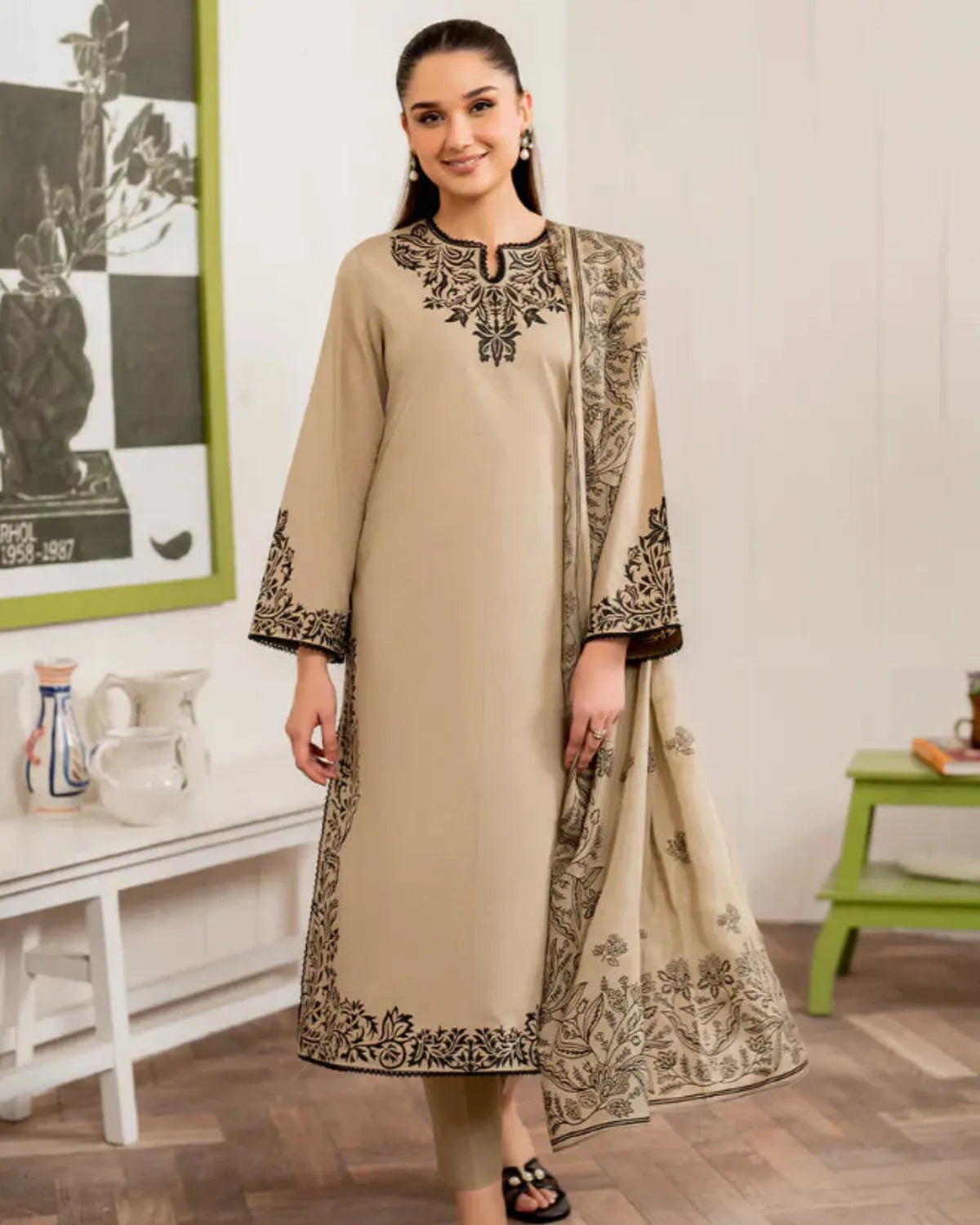 Woman wearing a beige embroidered outfit in a room with a white wall and green table.