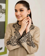 Woman wearing a beige blouse with black lace details, posing indoors.