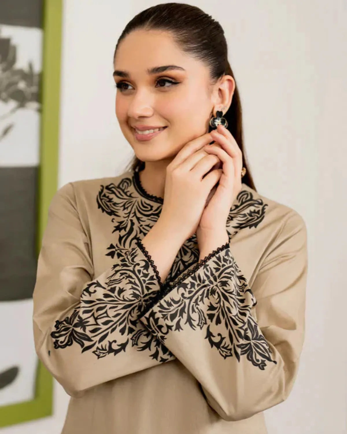 Woman wearing a beige blouse with black lace details, posing indoors.