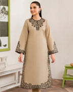 Woman wearing a beige dress with black embroidery in a room setting.