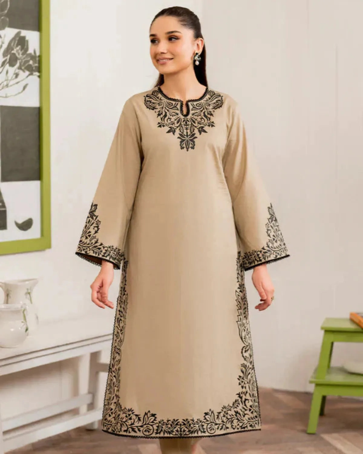 Woman wearing a beige dress with black embroidery in a room setting.