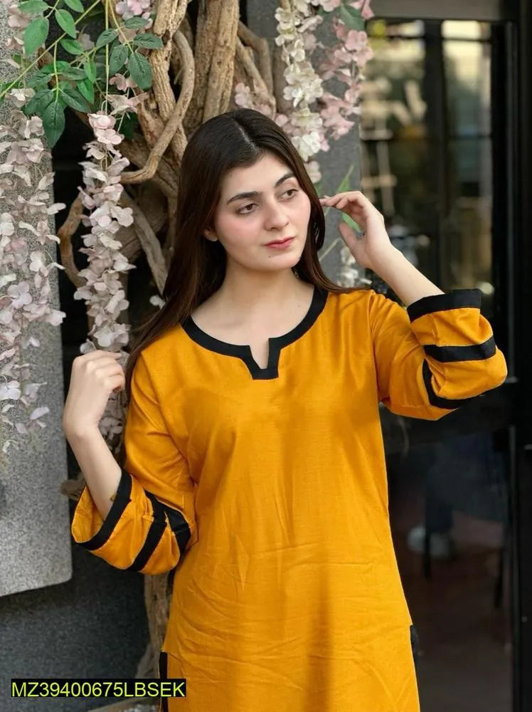 Woman wearing a yellow kurta with black trim in an outdoor setting with floral decorations.