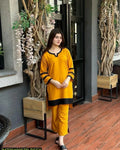 Woman in a yellow outfit standing in an indoor setting with plants and wooden furniture.