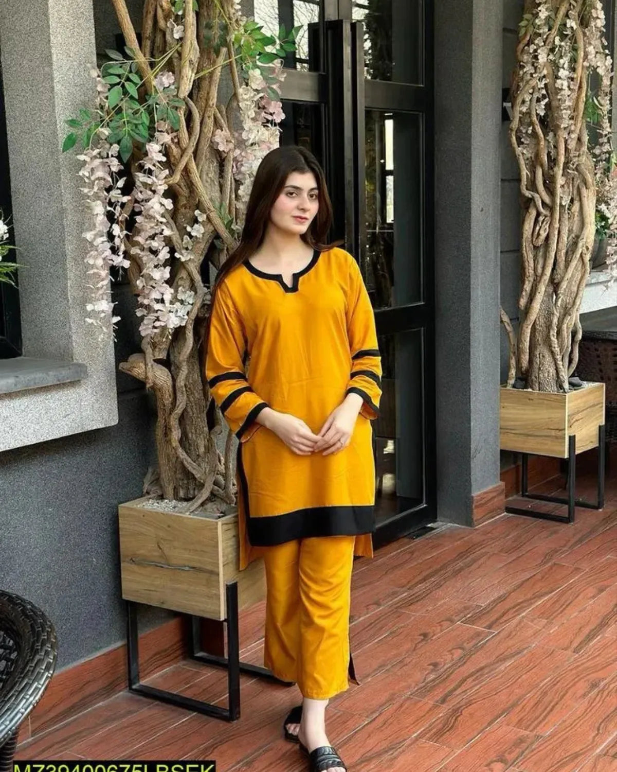Woman in a yellow outfit standing in an indoor setting with plants and wooden furniture.